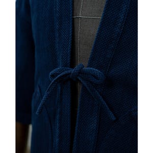 May include: A dark blue cotton jacket with a tie closure. The jacket has a textured weave and a relaxed fit.
