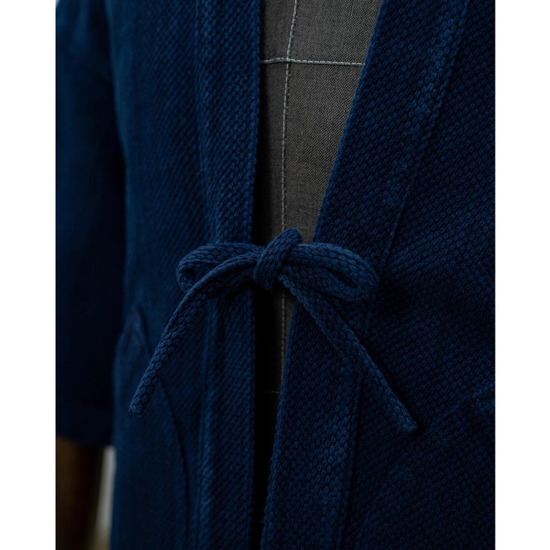 May include: A dark blue cotton jacket with a tie closure. The jacket has a textured weave and a relaxed fit.