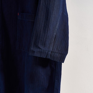 May include: Close-up of a dark blue denim jacket with a single pocket and a red accent. The jacket has long sleeves and is made of a textured fabric. The garment is likely part of a clothing collection.