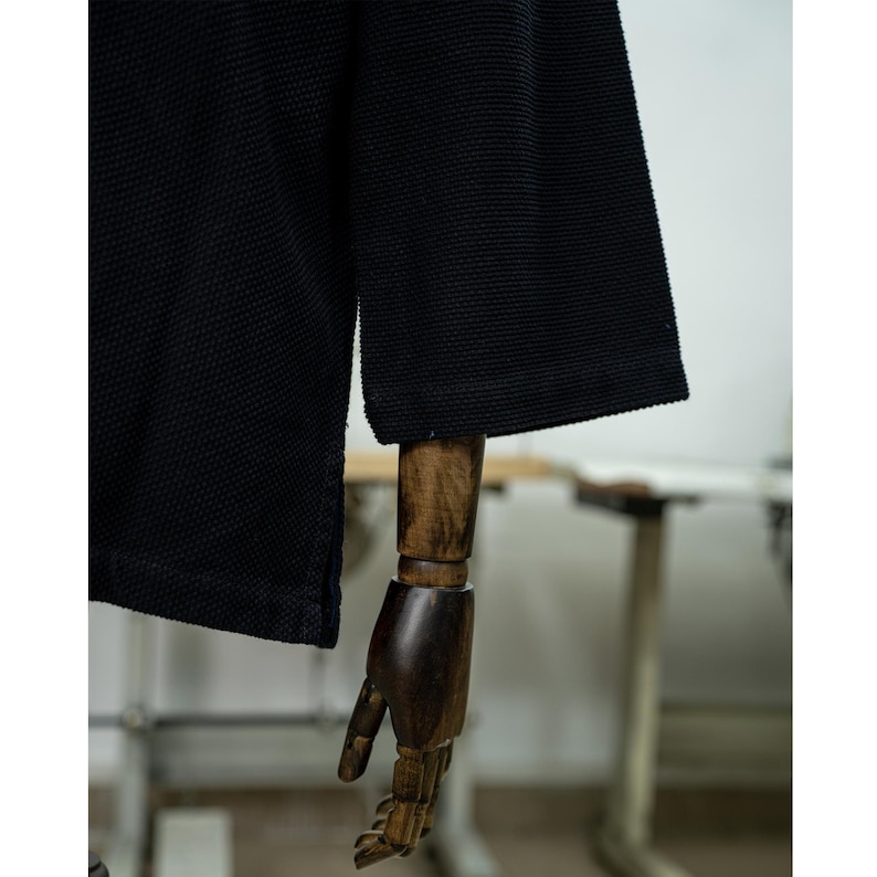 May include: A black long-sleeved shirt with a textured waffle knit fabric. The shirt is on a wooden mannequin.