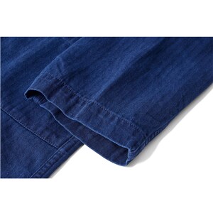 May include: Close-up of a section of blue denim fabric, showcasing the texture and stitching details. The image highlights the folded hem of a garment, likely pants or a jacket, with visible seams and a clean finish.