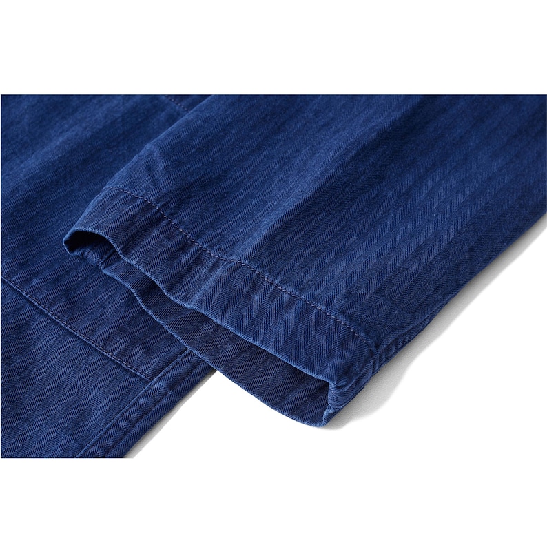 May include: Close-up of a section of blue denim fabric, showcasing the texture and stitching details. The image highlights the folded hem of a garment, likely pants or a jacket, with visible seams and a clean finish.