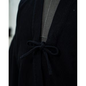 May include: A black cotton kimono with a tie closure at the front. The kimono is made of a textured fabric and has a relaxed fit.