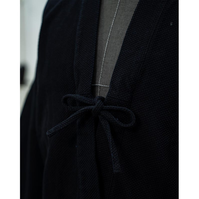 May include: A black cotton kimono with a tie closure at the front. The kimono is made of a textured fabric and has a relaxed fit.
