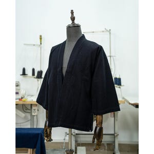 May include: A black cotton kimono jacket with a long, open front and three-quarter sleeves. The jacket is on a mannequin with wooden arms.