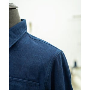 May include: Close-up of the shoulder and collar of a dark blue long-sleeved shirt. The fabric has a subtle texture.