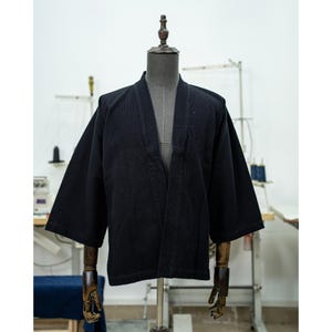 May include: A black, open-front jacket with long sleeves and a textured fabric. The jacket is displayed on a mannequin.