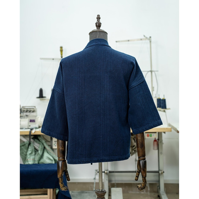 May include: A dark blue denim jacket with a textured weave. The jacket has a short sleeve and a relaxed fit.