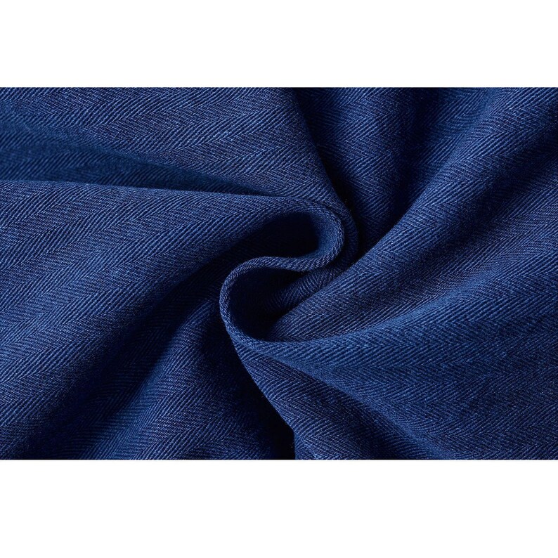 May include: Close-up of a deep blue fabric with a herringbone weave pattern. The fabric is folded, creating soft curves and shadows. The texture appears to be a medium weight, suitable for apparel or home decor.