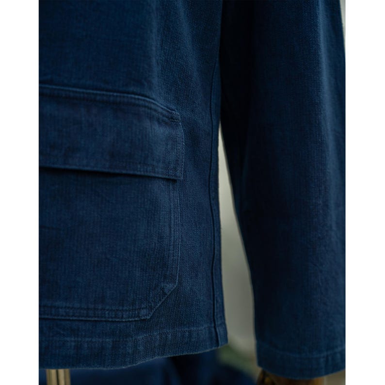 May include: A dark blue denim jacket with a large patch pocket on the front. The jacket has a corduroy texture and a relaxed fit.