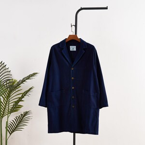 May include: A navy blue long coat with a classic collar and button-down front. The coat has two front pockets and is hanging on a black metal rack. The coat is made of a soft, durable fabric.