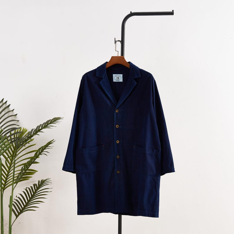 May include: A navy blue long coat with a classic collar and button-down front. The coat has two front pockets and is hanging on a black metal rack. The coat is made of a soft, durable fabric.