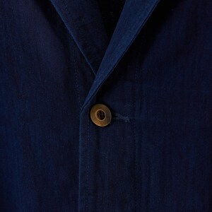 May include: Close-up of a navy blue blazer with a single, round, brass-colored button. The fabric has a subtle texture, and the button is centered on the jacket's front closure. The blazer's lapel is visible.