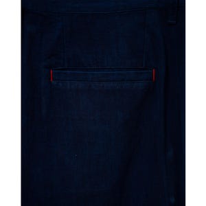 May include: Close-up of dark blue pants with a back pocket. The pocket has a red accent along the top edge. The fabric appears to be a sturdy, possibly denim, material.