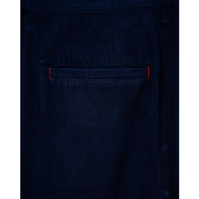 May include: Close-up of dark blue pants with a back pocket. The pocket has a red accent along the top edge. The fabric appears to be a sturdy, possibly denim, material.