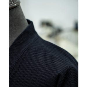 May include: Close-up of a dark blue, textured fabric with a collar. The fabric has a waffle-like texture.