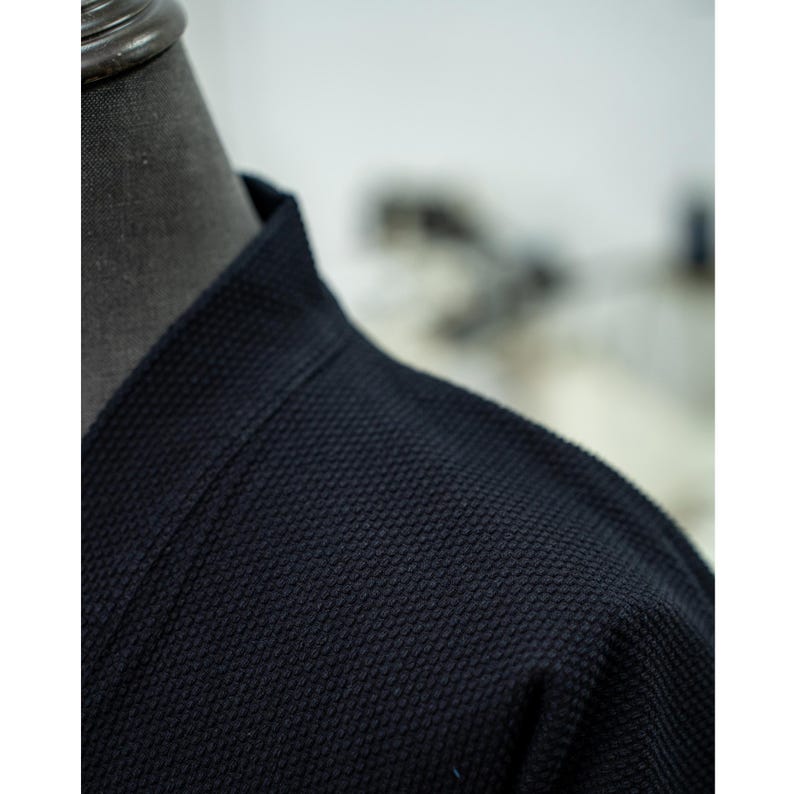 May include: Close-up of a dark blue, textured fabric with a collar. The fabric has a waffle-like texture.