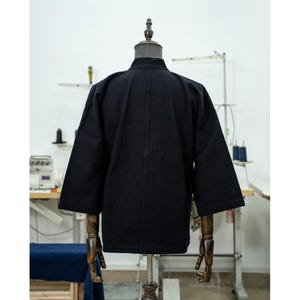 May include: A black cotton jacket with a stand-up collar and long sleeves. The jacket is unbuttoned and has a relaxed fit.