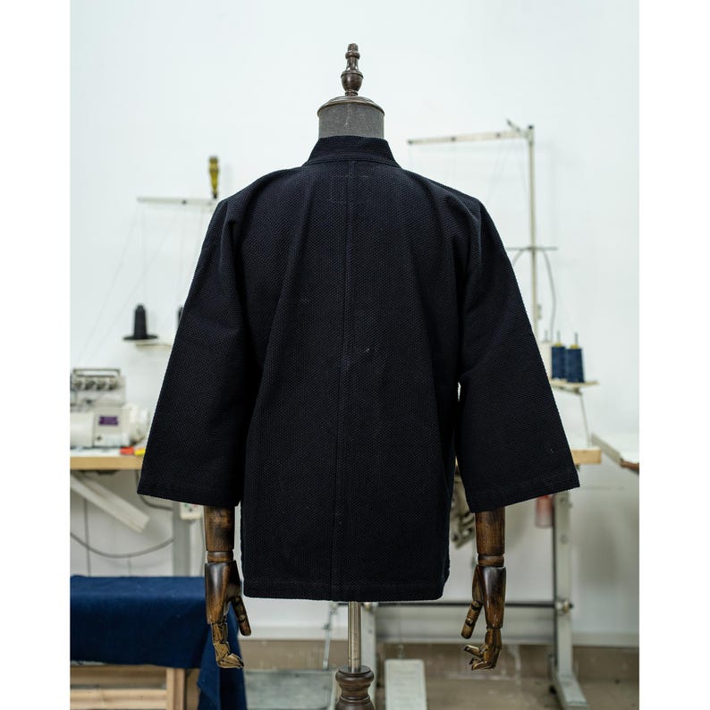 May include: A black cotton jacket with a stand-up collar and long sleeves. The jacket is unbuttoned and has a relaxed fit.