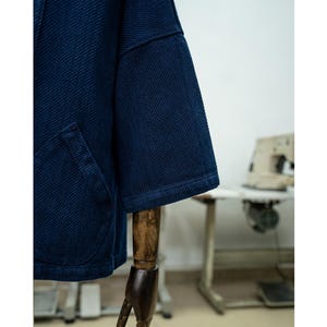 May include: A dark blue denim jacket with a waffle texture. The jacket has a long sleeve and a pocket on the left side.