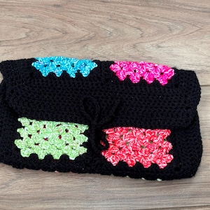 May include: A black crocheted clutch bag with colourful squares. The squares are made of green, blue and pink yarn.