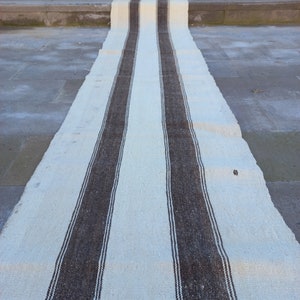 May include: A long, white runner rug with thick, brown stripes. The rug is made of a woven fabric and has a rustic, vintage look.