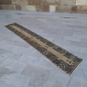 Pode incluir: Um tapete corredor bege e castanho com um padrão geométrico. O tapete está colocado sobre um piso de ladrilhos de cor cinza claro.