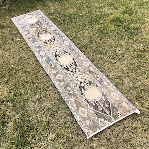 Könnte beinhalten: Ein langer, schmaler Teppich mit traditionellem persischem Design. Der Teppich hat einen cremefarbenen Hintergrund mit braunen, schwarzen und roten Akzenten. Der Teppich ist aus Wolle und hat an beiden Enden Fransen.
