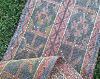 May include: A vintage runner rug with a geometric pattern in shades of pink, gray, blue, and green. The rug has a distressed look and is made of woven fabric.