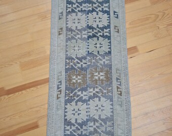 Puede incluir: Una alfombra de pasillo vintage con un patrón geométrico en tonos azules, marrones y blancos. La alfombra tiene un borde de flecos.