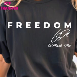 May include: Black t-shirt with the word "FREEDOM" in large white capital letters. Below the word is a white signature and the name "CHARLIE KIRK". The shirt is a crew neck style.