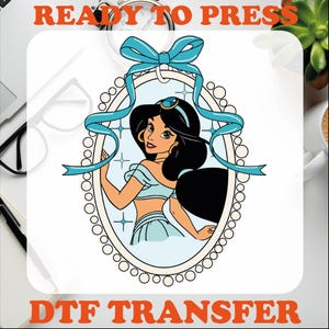 May include: A blue and white illustration of Princess Jasmine from Disney's Aladdin. She is standing in a round frame with a blue ribbon and pearl accents. The text "READY TO PRESS" is at the top of the image and "DTF TRANSFER" is at the bottom.