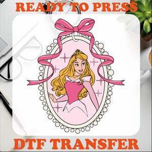 May include: A pink and white DTF transfer design featuring a cartoon image of Princess Aurora from Sleeping Beauty. The princess is wearing a pink dress and has long blonde hair. She is surrounded by pink ribbons and stars.