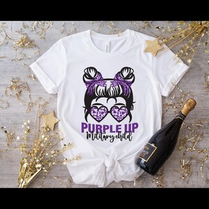 Peut inclure: T-shirt blanc avec un graphique violet d'une fille avec des couettes portant des lunettes de soleil et le texte "Purple Up Military Child".