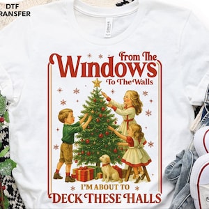May include: White t-shirt featuring a vintage-style Christmas graphic. The design includes the text "From The Windows To The Walls, I'm About To Deck These Halls" with illustrations of children decorating a Christmas tree and a dog.