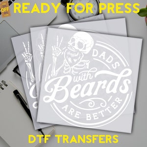 K&ouml;nnte beinhalten: Wei&szlig;e Vinylfolien mit einem Design eines Skeletts mit Bart und dem Text "Dads with Beards are Better" in einem Kreis. Der Text "DTF Transfers" befindet sich am unteren Rand des Bildes.