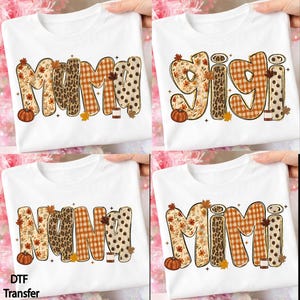 May include: A white t-shirt featuring a graphic design with the word MAMA, GIGI, NANA, or MIMI. Each letter has a unique pattern including autumn leaves, leopard print, orange plaid, and brown polka dots, accented with a small pumpkin.