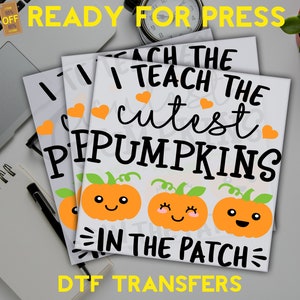 May include: Stacked white DTF transfer sheets with the text "I teach the cutest pumpkins in the patch" and three orange pumpkin illustrations. The words "READY FOR PRESS" and "DTF TRANSFERS" are also visible.