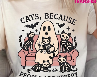 May include: Cream-colored t-shirt with a Halloween-themed graphic. The design features a ghost, skeleton cats, bats, and the text "CATS, BECAUSE PEOPLE ARE CREEPY". The cats are sitting on a pink couch.