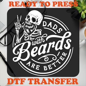 K&ouml;nnte beinhalten: Schwarzwei&szlig;es Grafikdesign mit einem Sch&auml;del mit Bart und dem Text "Dads with Beards are Better" in einem Kreis. Die Texte "Ready to Press" und "DTF Transfer" sind oben und unten im Bild orange.