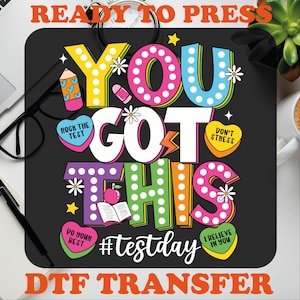 May include: A black and white graphic design with the text "You Got This" in colorful letters with white polka dots. The text is surrounded by hearts, stars, and flowers. The text "#testday" is below the main text. The text "READY TO PRESS" is at the top of the image and the text "DTF TRANSFER" is at the bottom of the image.