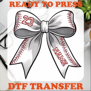 May include: A white bow design with baseball stitching and the text "NAME" and the number "23" in red. The words "READY TO PRESS" and "DTF TRANSFER" are in orange text.