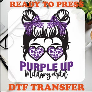 Peut inclure: Design de transfert DTF Purple Up Military Child avec une fille de dessin anim&eacute; portant des lunettes de soleil en forme de c&oelig;ur violet et des n&oelig;uds. Le design est pr&ecirc;t &agrave; &ecirc;tre press&eacute;.
