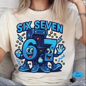 May include: Cream-colored t-shirt featuring a playful graphic of the numbers "6" and "7" as cartoon characters, with the text "SIX SEVEN" above them in blue. The design includes lightning bolts and a retro arcade machine.