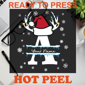 May include: A black graphic with a white letter "A" decorated with a Santa hat and antlers, snowflakes, and the text "Your Name". The words "READY TO PRESS" and "HOT PEEL" are in orange.
