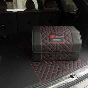 May include: Black car trunk organizer and floor mat set with red diamond stitching. The organizer has a flap closure and a red and silver emblem. The set is in a car trunk.