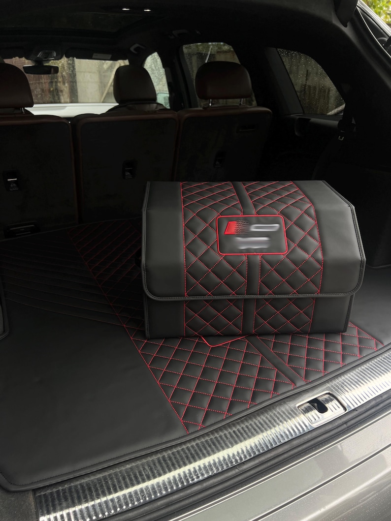 May include: Black car trunk organizer and floor mat set with red diamond stitching. The organizer has a flap closure and a red and silver emblem. The set is in a car trunk.