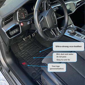 May include: Black car floor mats made of eco-leather with a textured surface. The mats are designed to be water, dirt, and dust resistant. The mats feature a logo that can be personalized.