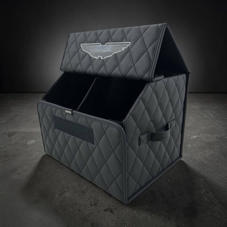 May include: A black, quilted storage organizer with a divided interior and a hinged lid. The organizer features a diamond pattern, a handle, and a logo on the lid. The organizer is designed for car storage.