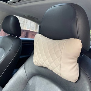 May include: Beige quilted headrest pillow for a car seat. The pillow is designed to provide comfort and support for the head and neck.